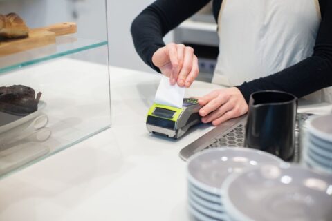 Retail worker printing a receipt beside a pastry display and card terminal